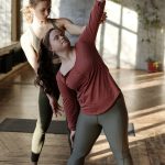 Inclusive yoga session with a female trainer assisting a woman with Down syndrome in a studio setting.